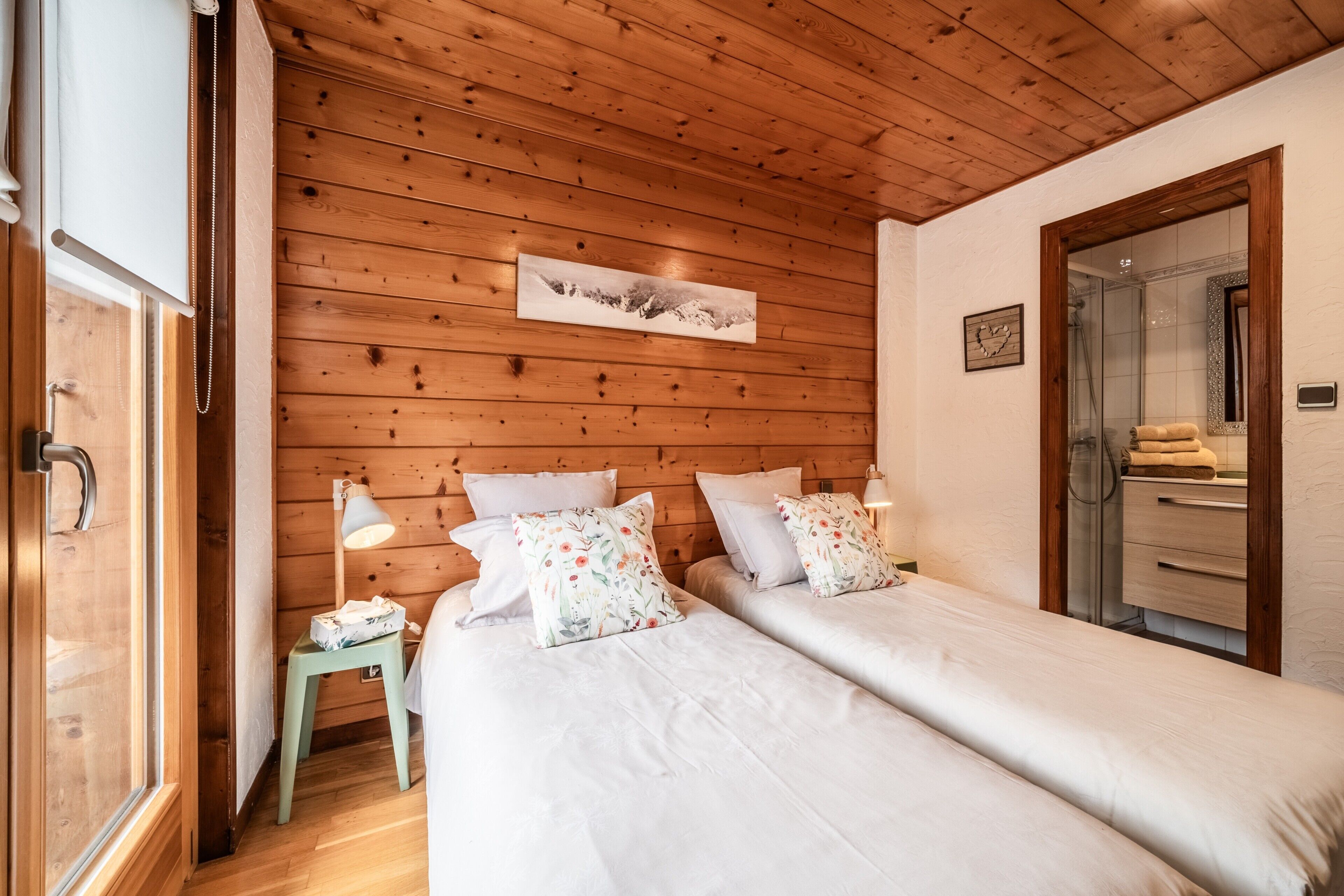 A wooden-paneled room with two beds, a small table, a lamp, and a mirror.
