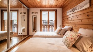 Een slaapkamer met houten plafond, twee bedden, een grote spiegel en een balkon met uitzicht.