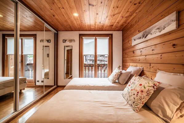 Une chambre avec un plafond en bois, deux lits, un grand miroir et un balcon avec vue.