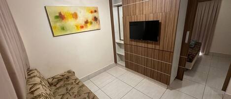 A living room with a sofa, a TV mounted on a wooden wall, and a ceiling fan.