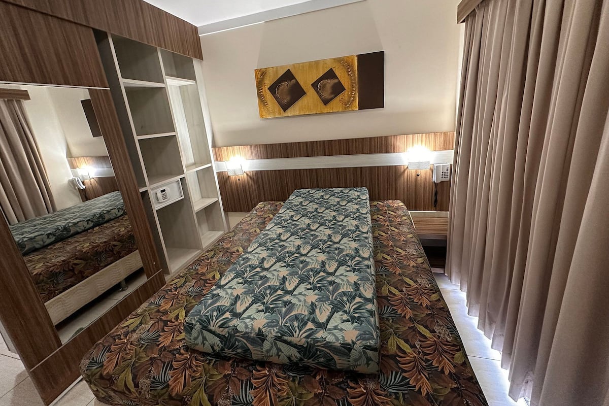 Une chambre d’hôtel équipée d’un lit, d’une armoire, d’un miroir et d’un téléphone fixé au mur.