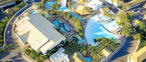 An aerial view of a resort with multiple swimming pools, a central building, and a parking area.