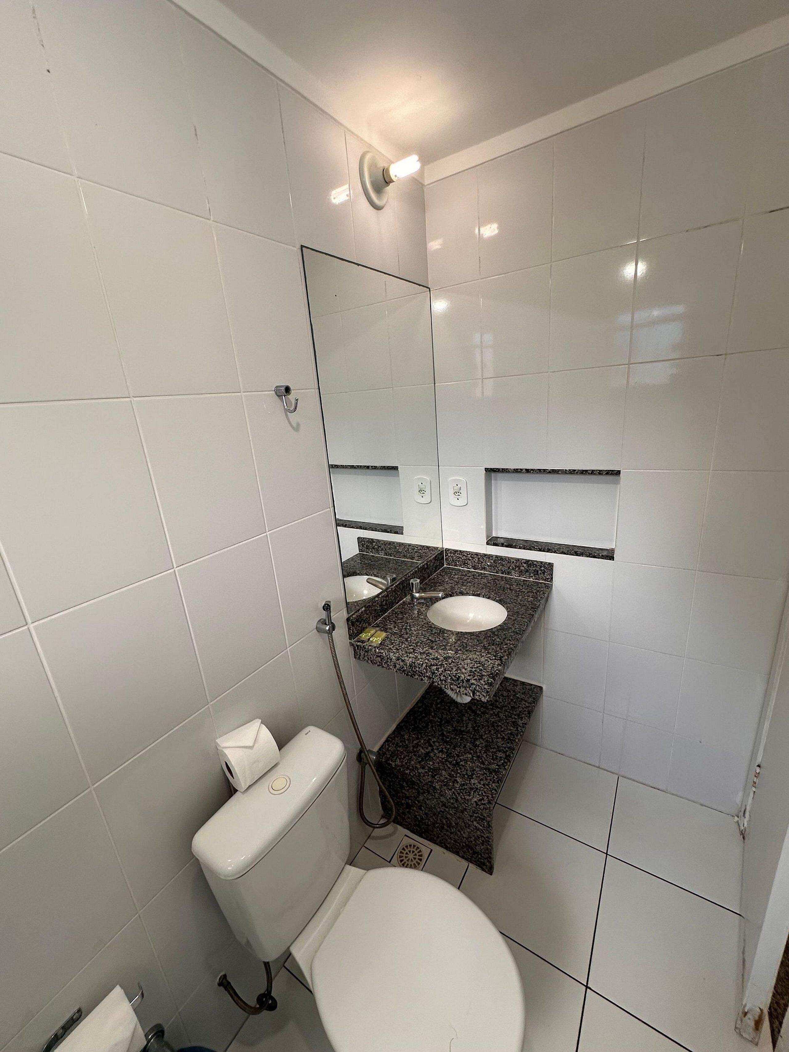 Un baño con azulejos blancos, un inodoro, un lavabo con espejo y una zona de ducha.