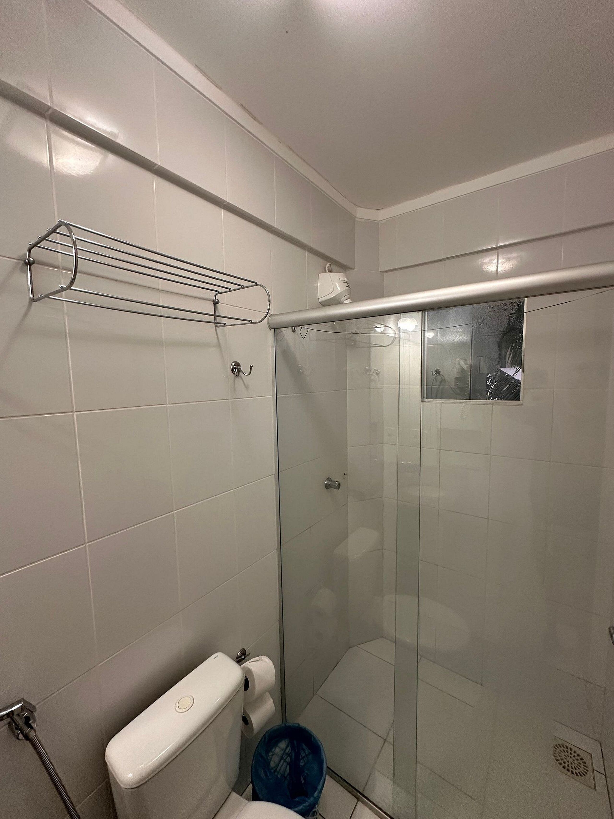 Et lille, moderne badeværelse med hvide fliser, en glasbrusekabine, et toilet og en blå skraldespand.