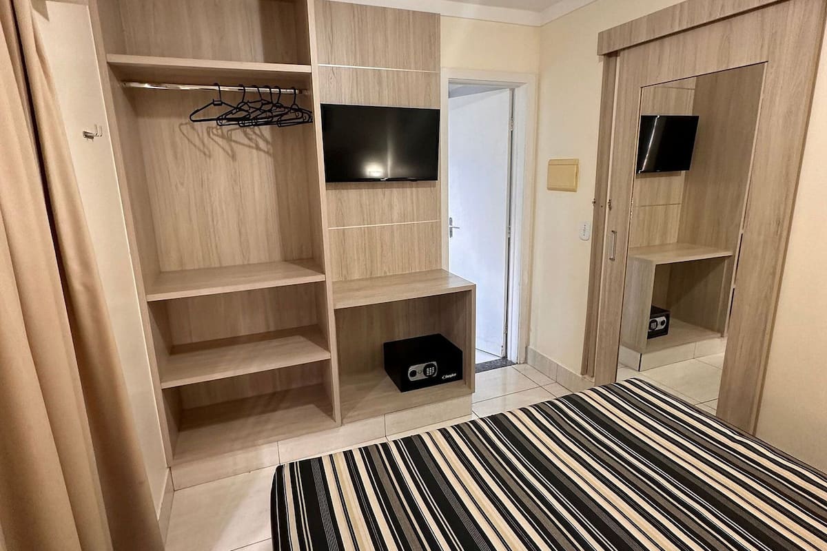 Une chambre d’hôtel comprenant un lit, un téléviseur fixé au mur, une armoire avec des étagères et un petit meuble de rangement.