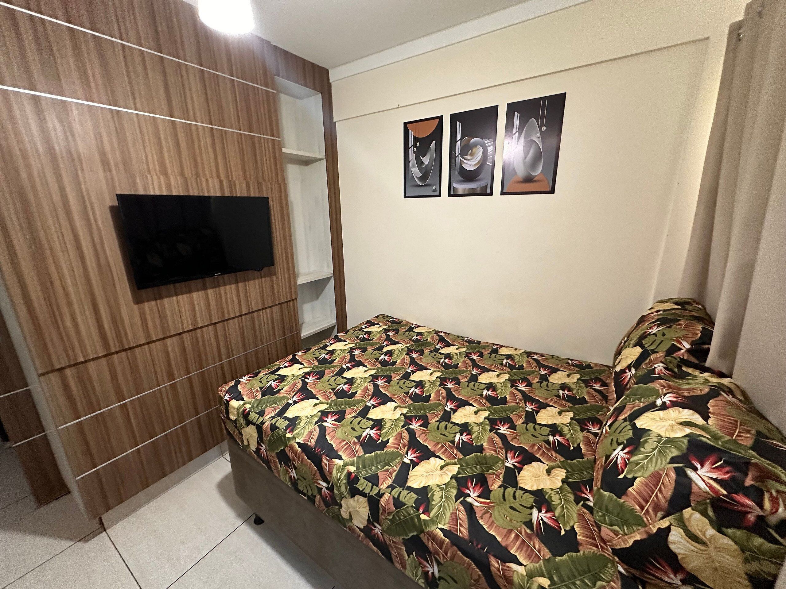A bedroom with a bed, a television mounted on a wooden panel wall, and three framed pictures on the wall.