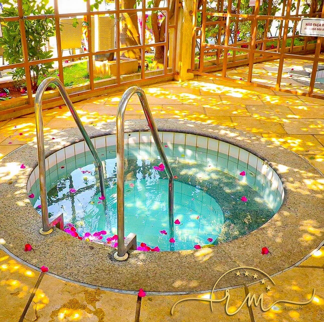 A hot tub with metal steps and a tiled edge, surrounded by a stone floor and a wooden fence.
