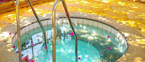 A hot tub with metal steps and a tiled edge, surrounded by a stone floor and a wooden fence.
