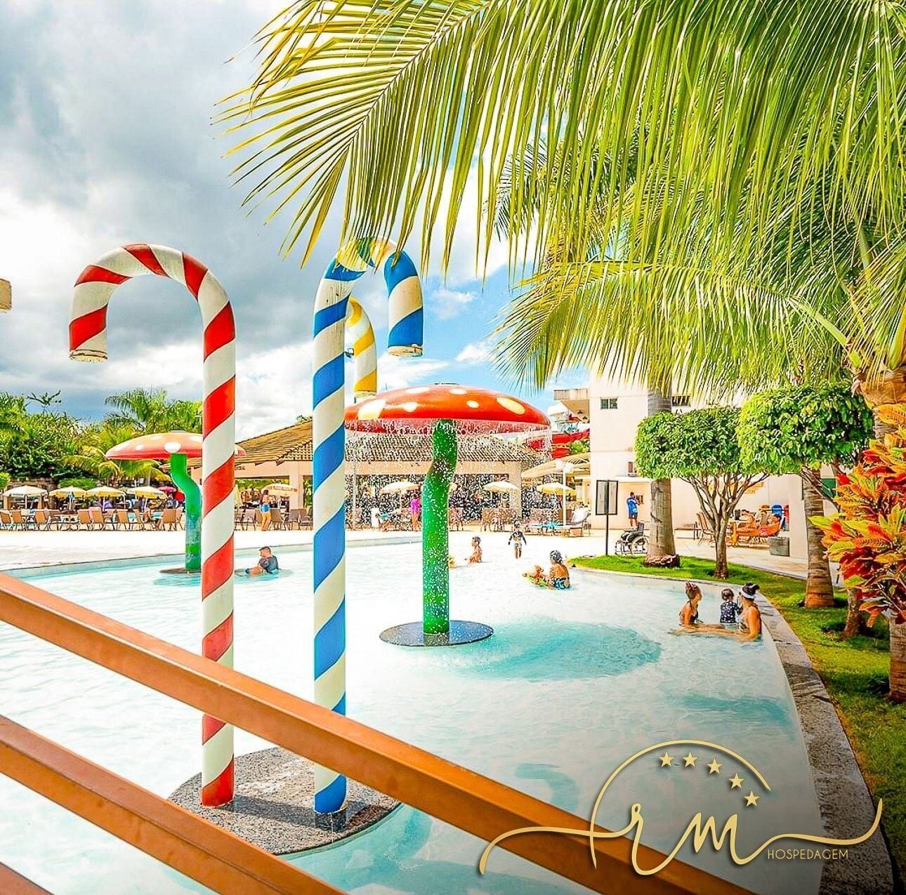 A pool area with striped poles, umbrellas, and palm trees.