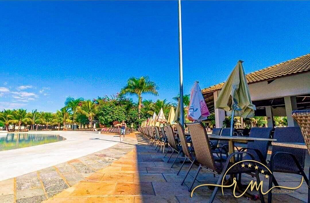 Ein Poolbereich einer Hotelanlage mit Liegestühlen und Sonnenschirmen, umgeben von Palmen und blauem Himmel.