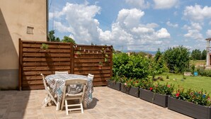 Un patio exterior con una mesa y sillas, una valla de madera y un jardín lleno de flores.