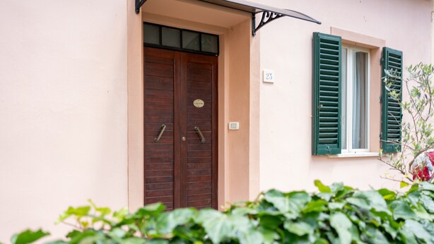 Un edificio con una puerta doble de madera, una ventana con contraventanas verdes y el número 23 en la pared.