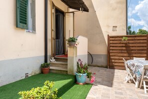 A patio with artificial grass, a wooden table with a patterned tablecloth, and potted plants.