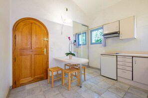 A kitchen with a wooden door, a round table with chairs, a potted plant, and white cabinets. - Peaceful Villa "Numéro 2" with Private Pool and HD Wi-Fi (Châteauneuf-Grasse)
