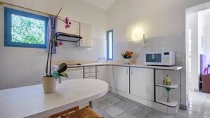 Una cocina moderna con armarios blancos, microondas, pileta y comedor con mesa y sillas.