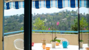A balcony with a table set for two, a striped awning, and a view of a hilly landscape.
