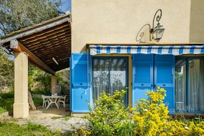 Un bâtiment aux volets bleus, doté d’un patio couvert et d’un mur en pierre.