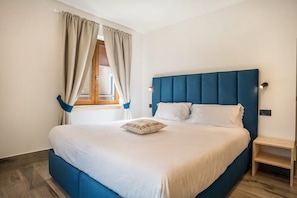 Een slaapkamer met een groot bed, een houten hoofdbord, een nachtkastje en een raam met gordijnen.