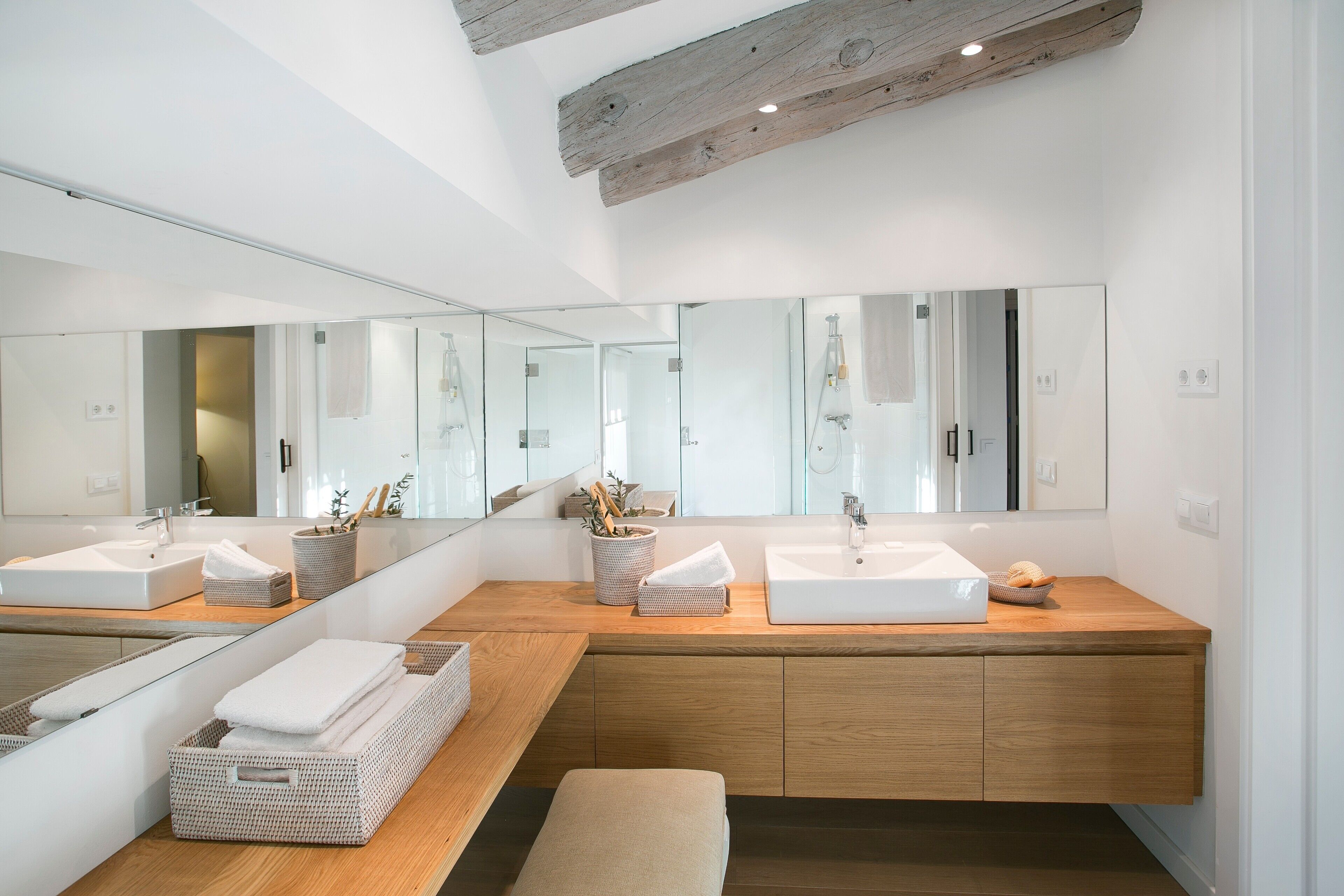A modern bathroom with two sinks, a large mirror, wooden cabinets, and a bench.