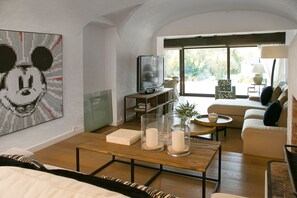 Una sala de estar con televisión, una mesa de centro con velas, un sofá y una gran obra de arte de Mickey Mouse en la pared.