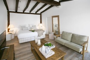 Un dormitorio con cama, mesitas de noche, un banco de madera, un sofá y un espejo.