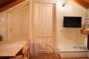 A room with a wooden dining table, two wooden doors, a stone wall, a mounted flat-screen TV, and a stone fireplace. - Holiday Home 'Il Piccolo Sogno' with Mountain View and Wi-Fi (Temu’)