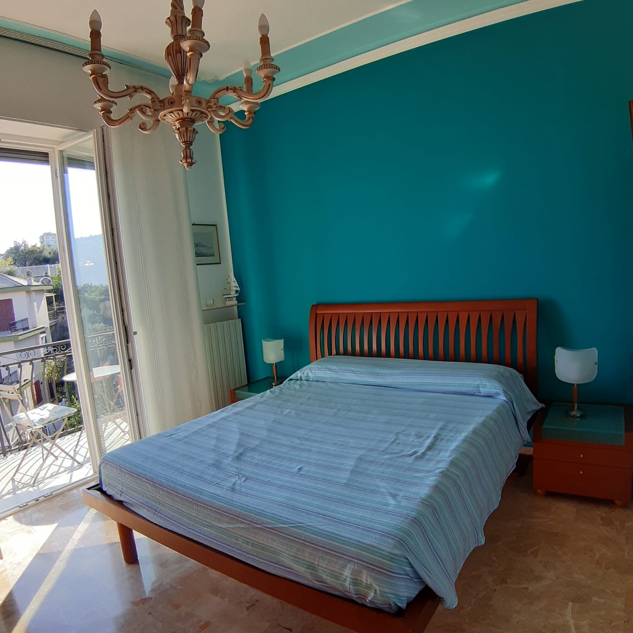 Un dormitorio con cama, mesita de noche, lámpara, candelabro y vistas a través de una ventana.