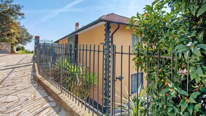 Ein Haus mit einem Kiesweg, einem Metallzaun und einem Garten mit Orangenbäumen.