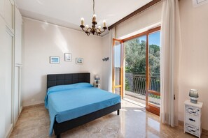 Une chambre à coucher avec un lit, un lustre, une table de chevet, une fenêtre et un balcon.