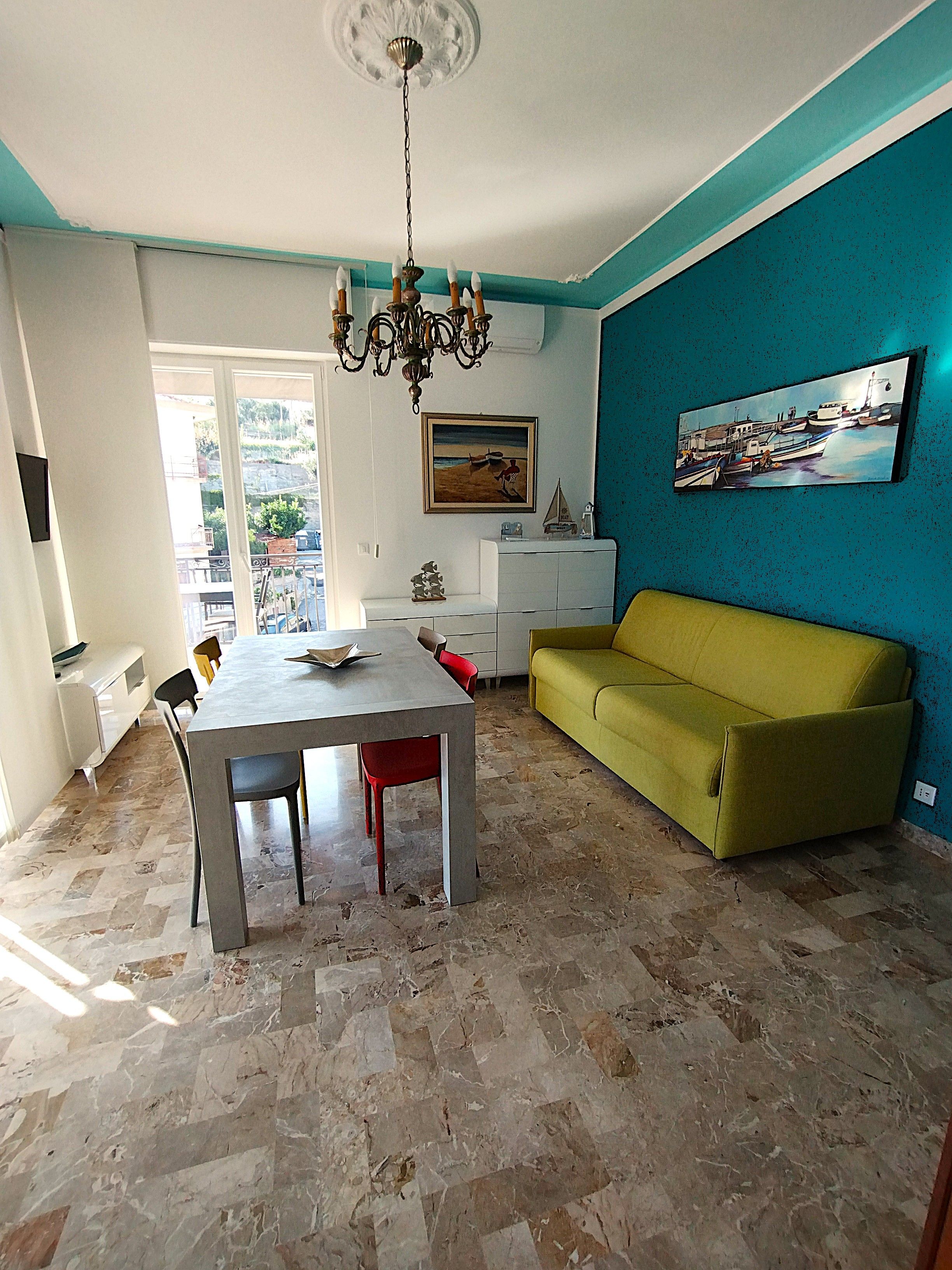 A dining area with a table and chairs, a sofa, a chandelier, and artwork on the walls.