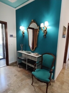 A room with teal walls, a wooden chair, a white console table with a mirror and wall sconces, and a door leading outside.