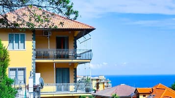 Un edificio de varios pisos con balcones, vista despejada al mar y un muro de piedra en primer plano.