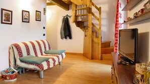 Ein gemütliches Zimmer mit einer Holztreppe, einem Sofa, einem Fernseher und einem Tisch mit Gegenständen.