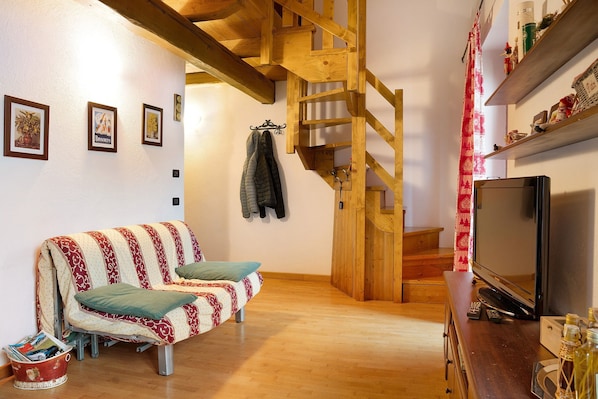 A cozy room with a wooden staircase, a sofa, a TV, and a small table with items.