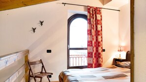 Ein Schlafzimmer mit Bett, Sessel, Fenster mit Vorhängen, Nachttisch und Lampe.
