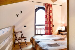A bedroom with a bed, a chair, a window with curtains, a nightstand, and a lamp. - Apartment 'Casa Sul Fiume' with Mountain View, Balcony and Wi-Fi (Vernante)