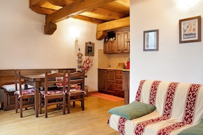 A dining area with a wooden table and chairs, a kitchen with wooden cabinets, and a patterned sofa.