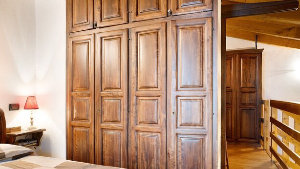 Ein Schlafzimmer mit einem Bett, einem Holzschrank, einem Nachttisch, einer Lampe und einem Flur mit Holzbalkon.