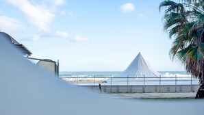 A beach view with a tent-like structure, a palm tree, and a clear sky.