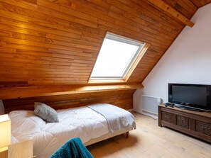 A bedroom with a sloped ceiling, a skylight, a bed, a TV, and a wooden dresser.