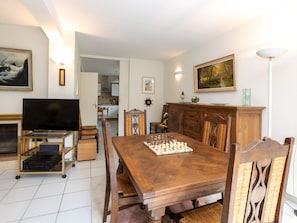 A dining area with a wooden table set for two, a chessboard, and a television on a stand.