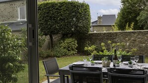 Een terras buiten met een eettafel, omringd door stenen muren en groen.