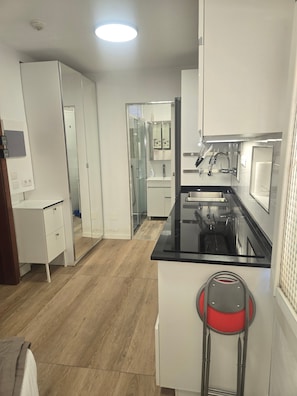 A modern kitchen with a black countertop, stainless steel appliances, and a glass door leading to a bathroom.