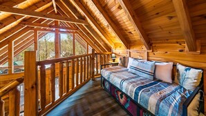Un chalet confortable avec un intérieur en bois, une chambre en mezzanine dotée d’un lit et offrant une vue sur l’extérieur.