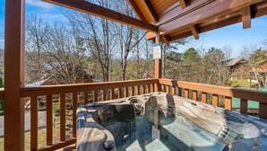 Un bain à remous installé sous une terrasse en bois, avec vue sur les arbres et les maisons.
