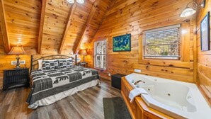 Une chambre située dans une cabane en rondins, avec un grand lit, une baignoire et une fenêtre équipée de stores.