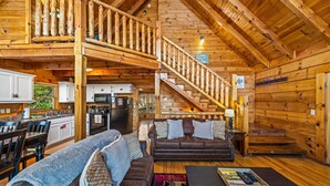 L’intérieur de la cabane comprend un escalier en bois, un coin cuisine, un salon avec un canapé et une table basse, ainsi qu’un coin repas avec des chaises et une table.