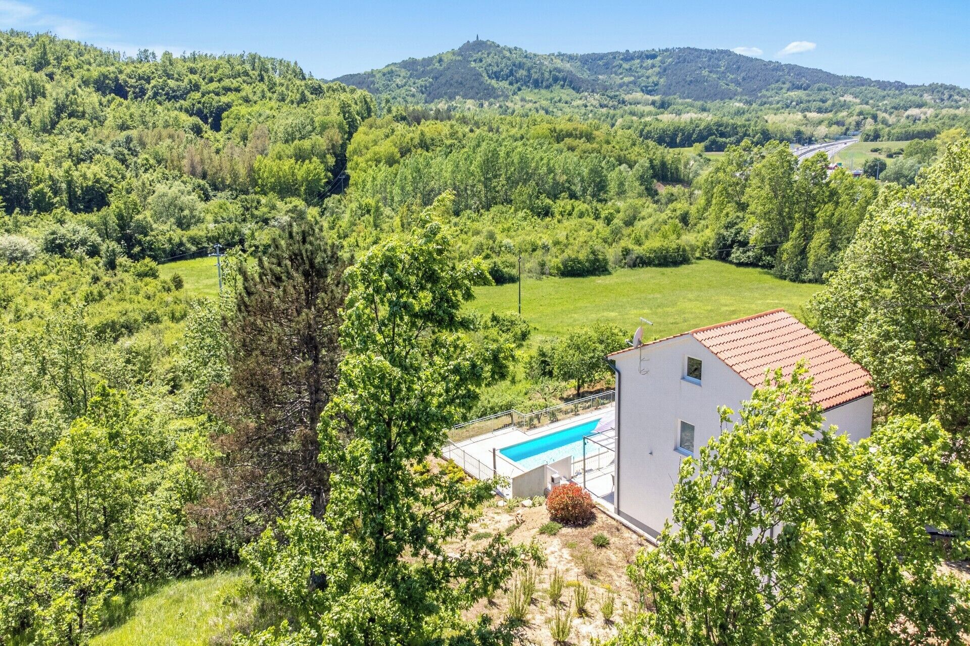 Une maison avec une piscine, entourée d’une végétation luxuriante et de collines.