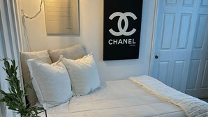 Ein Schlafzimmer mit einem Bett, einem Nachttisch mit Vase und Buch, einer Wandlampe und einer Tür.