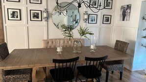 Ein Esszimmer mit Holztisch, schwarzen Stühlen, einer Chandelüster, gerahmten Fotos an der Wand und einem Spiegel.